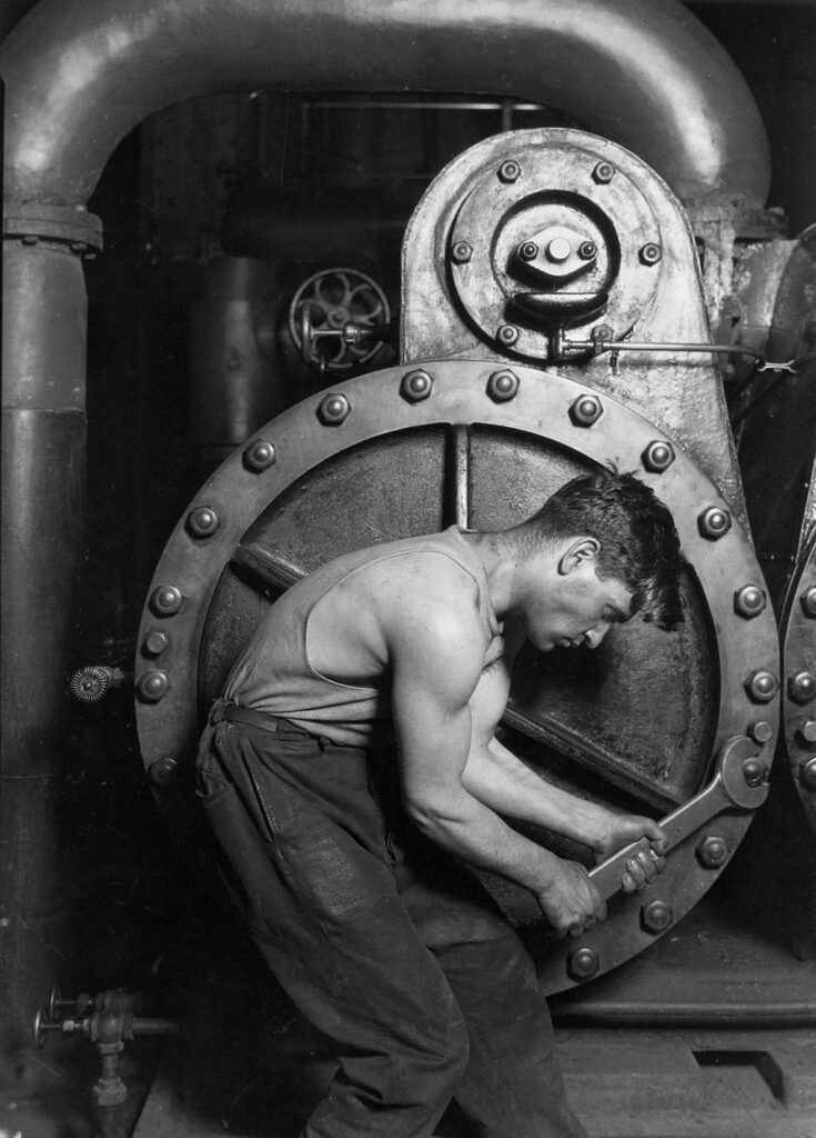 Ein Arbeiter kniet und arbeitet mit einem Werkzeug an der großen, verschraubten Flanschplatte einer industriellen Maschine.