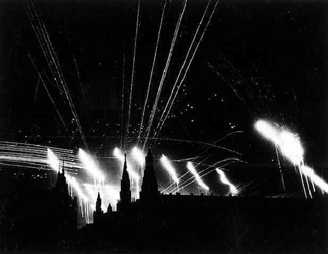 Mehrere Feuerwerke explodieren am Nachthimmel über einer dunklen Stadtsilhouette.